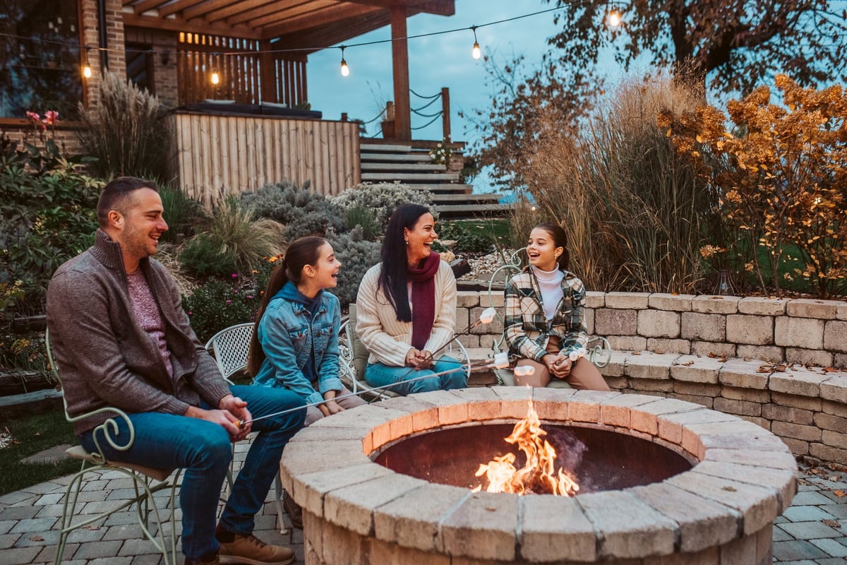 Family roasting marshmallows around fire pit at night, making smores together outdoors