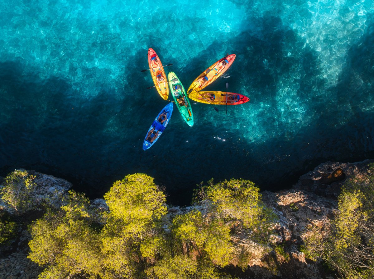 Aerial drone view of colorful kayaks with people paddling on crystal clear turquoise sea