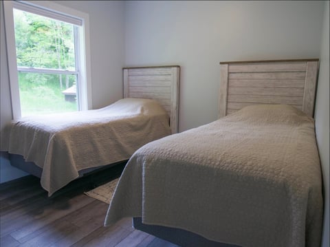 Two twin beds with wooden headboards in a bright bedroom with a window and hardwood floors