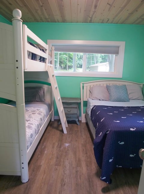 Bright green childrens bedroom with white bunk bed, single bed, wooden floor, and large window overlooking trees