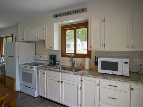 Modern kitchen with white cabinetry, stainless steel appliances, granite countertops, and wooden framed windows above the sink