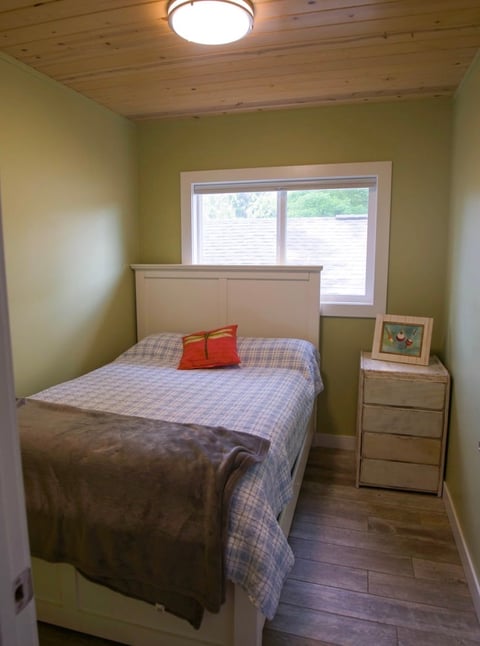 Cozy bedroom with yellow-green walls, queen bed with blue plaid bedding, nightstand, and sliding glass doors with window treatments