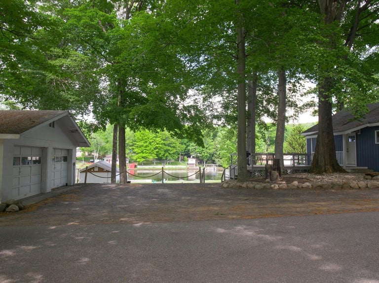 Gravel driveway with gray shed on left, tall trees, and park grounds visible through open area