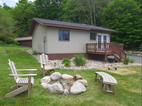 Small cabin with wooden deck surrounded by Adirondack chairs and a fire pit with large stones