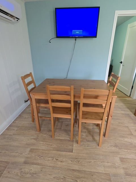 Wooden dining table with four chairs in a room with blue-painted walls and a wall-mounted TV displaying a blue screen