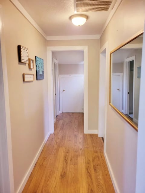 Hallway with cream walls, hardwood flooring, ceiling light fixture, framed mirror, and white doors leading to other rooms