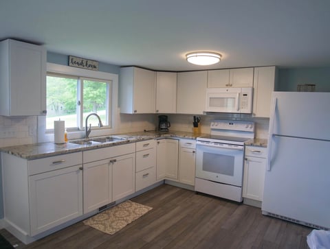 Modern kitchen with white cabinetry, stainless steel appliances, granite countertops, and dark wood-style flooring