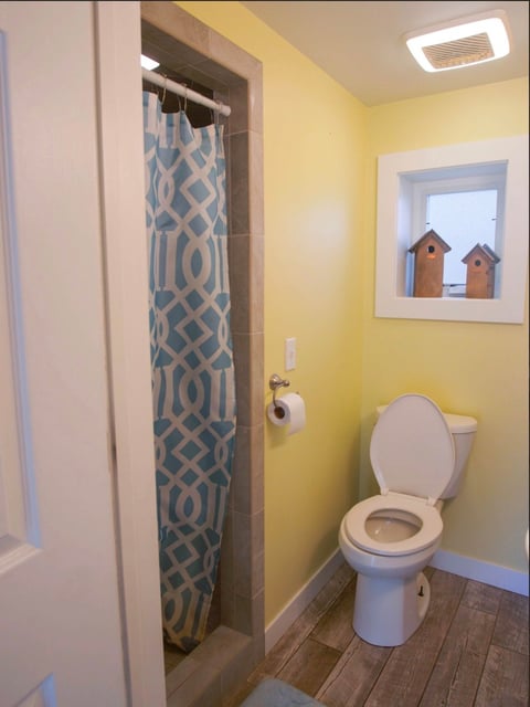 Bright yellow bathroom with white toilet, blue geometric shower curtain, and framed birdhouse artwork on wall