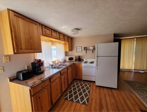 Kitchen with wooden cabinets, white refrigerator, electric stove, and hardwood flooring with geometric accent rug