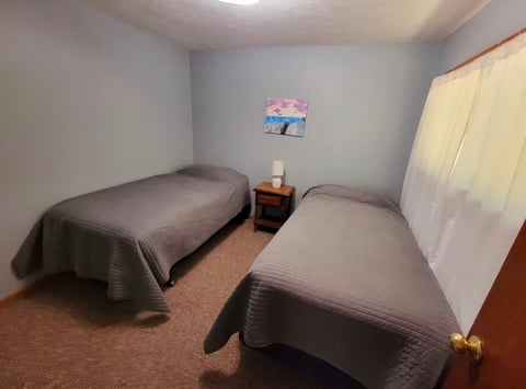 Small bedroom with two twin beds, wooden nightstand, and framed picture on gray wall