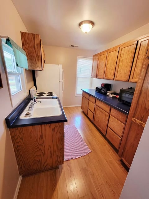 Galley-style kitchen with wood cabinets, black countertops, stovetop, sink, and hardwood flooring