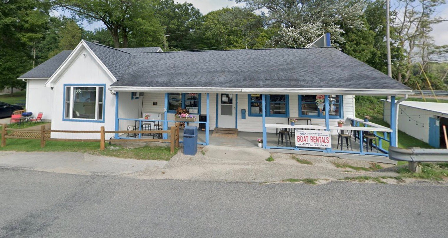 Small white commercial building with blue trim and covered porch, surrounded by trees