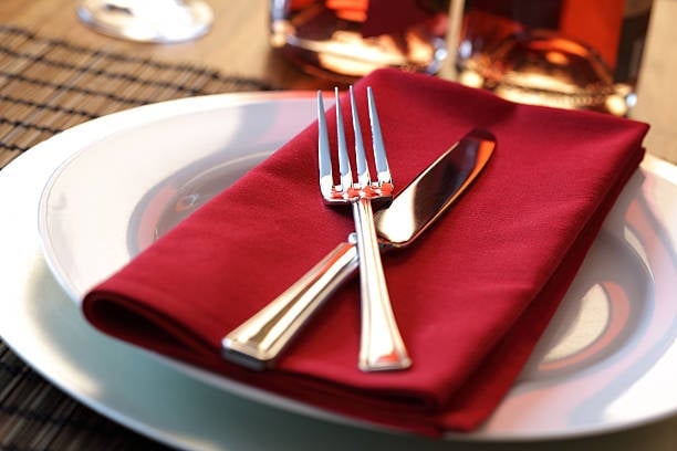 Elegant formal place setting with white plate, red napkin, and silver fork and knife on a striped placemat
