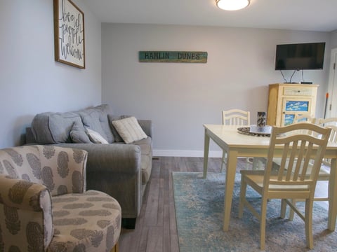 Cozy living room with gray sofa, patterned armchair, wooden desk with two chairs, TV, and framed wall art