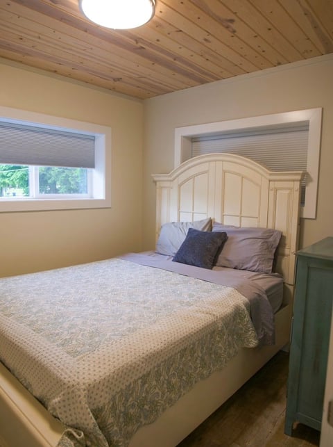 Cozy bedroom with cream-colored wooden bed, yellow walls, wood ceiling, window with blinds, and green storage unit