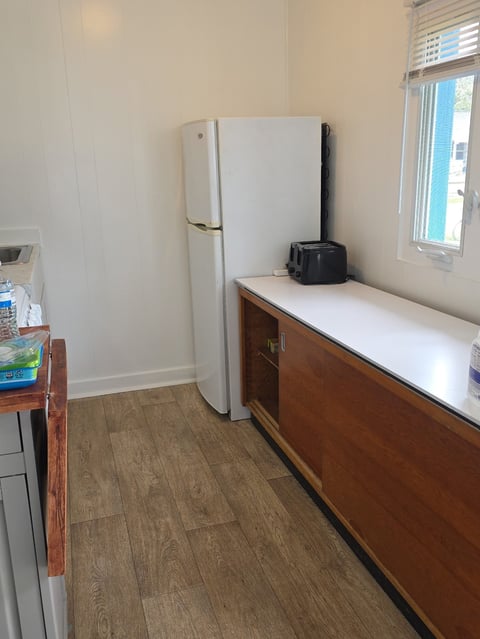 Small kitchen with white refrigerator, wooden counter, black coffee maker, window with blinds, and wood-look flooring