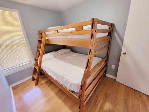 Wooden bunk bed with white mattresses in a bedroom with hardwood flooring and light blue walls