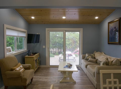 Modern living room with blue walls, wooden ceiling, beige seating furniture, and glass doors opening to a patio with trees