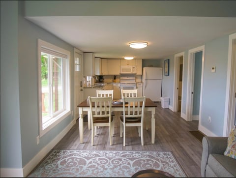 Open-concept kitchen and dining room with white dining table, chairs, light wood cabinets, and hardwood flooring