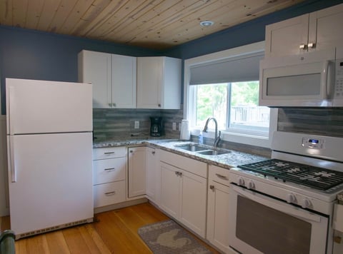 Modern kitchen with white cabinetry, stainless steel appliances, teal accent wall, and wooden ceiling