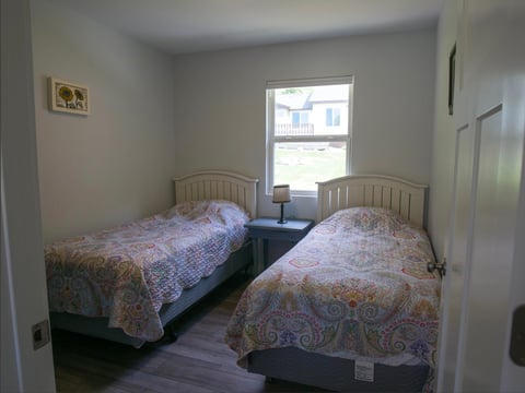 A bedroom with two twin beds with patterned bedding, a window, and beige walls with minimal furniture