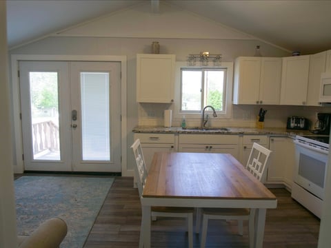 Bright kitchen with cream cabinets, wood dining island with two chairs, white appliances, and glass doors leading to a deck