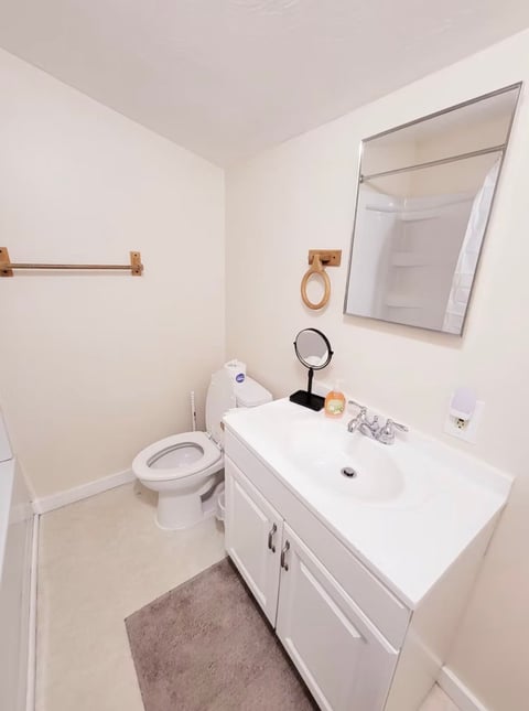 Modern bathroom with white vanity, mirror, toilet, and wood accents on light beige walls