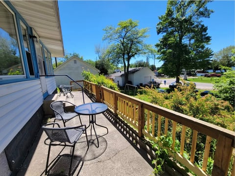 Elevated deck with wooden railing, patio furniture, and view of trees and residential area on clear day