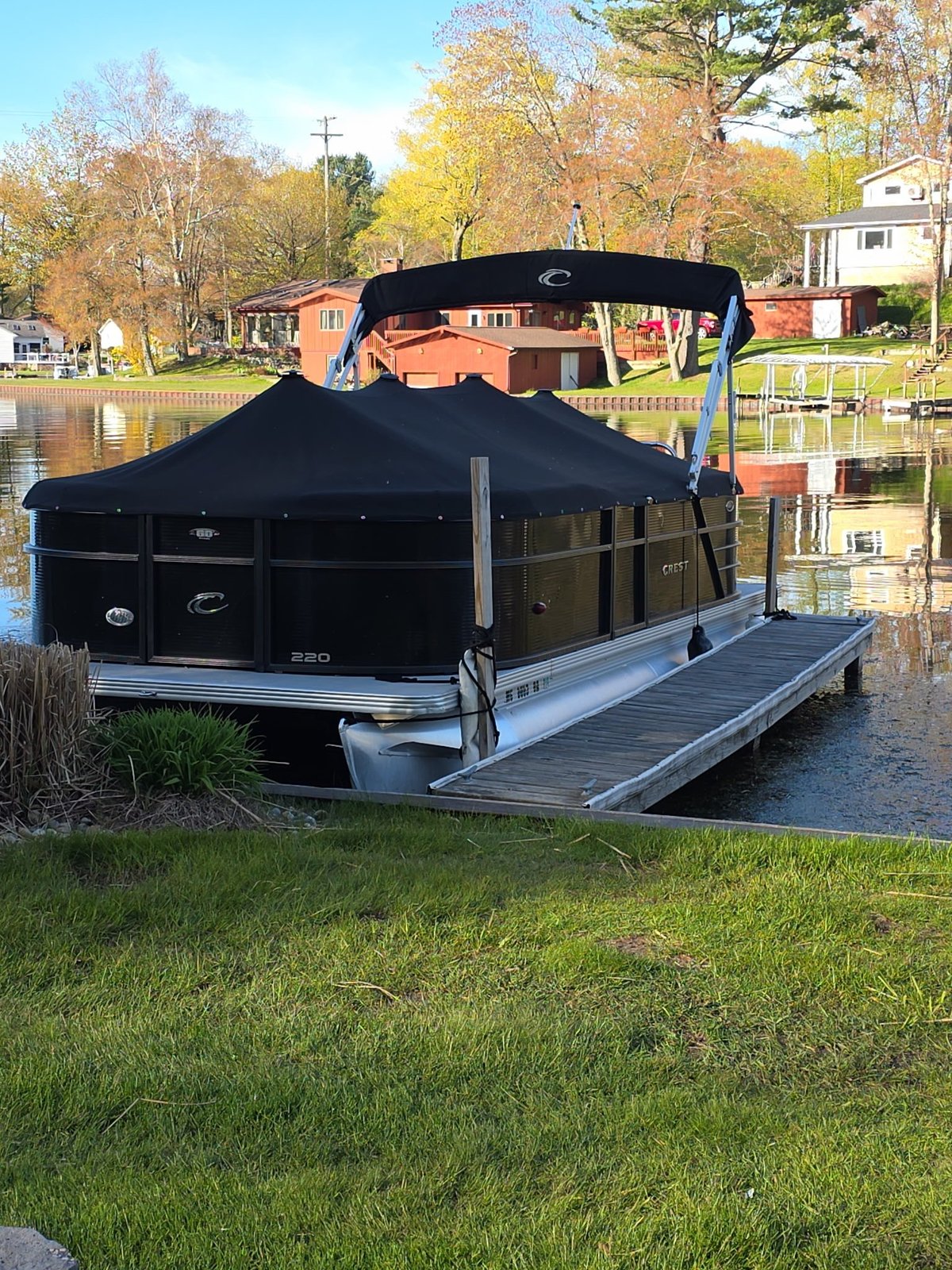 Black and orange pontoon boat docked at residential waterfront with autumn foliage in background
