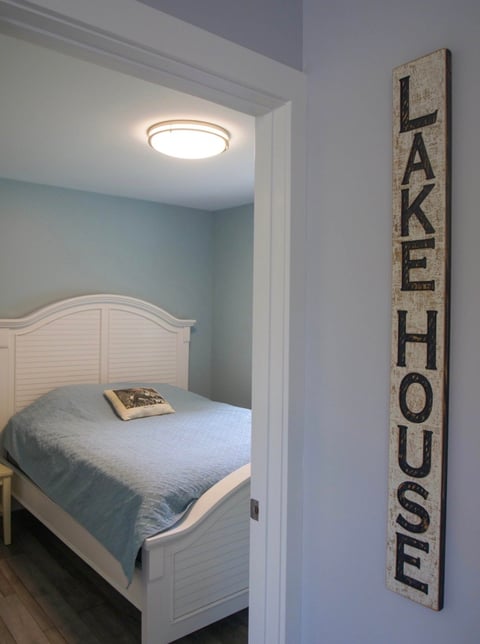 Bedroom doorway with white bed, blue walls, and wooden Lake House sign on white wall