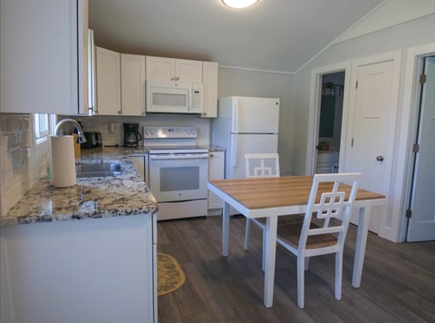 Open-concept kitchen and dining area with white cabinetry, stainless steel appliances, granite countertops, and a wooden dining table with white chairs