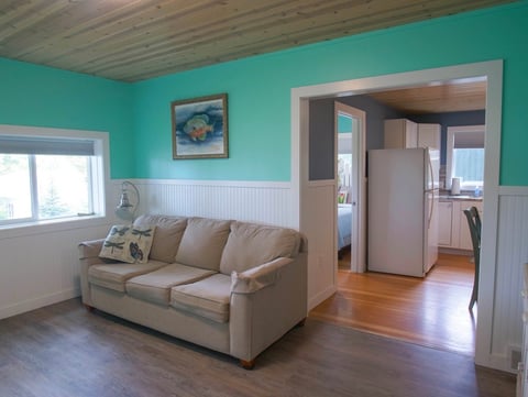 Turquoise living room with beige sofa, white wainscoting, hardwood floors, and doorway to kitchen