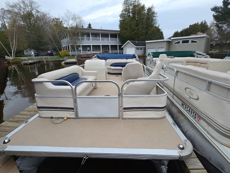 Beige pontoon boat docked at a waterfront property with residential buildings