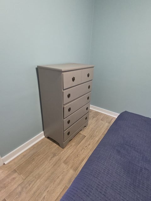 Gray five-drawer dresser with wooden handles positioned against a light blue wall next to a blue carpet and wooden floor