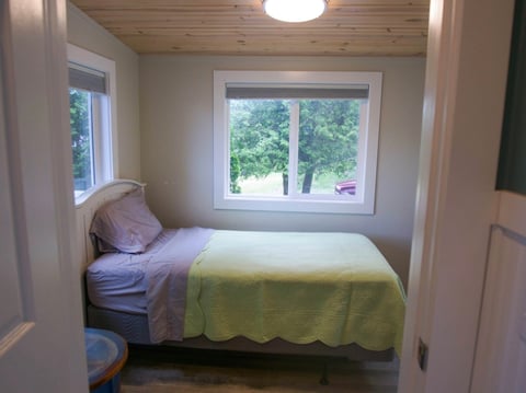 Small bedroom with a twin bed covered in yellow bedding, purple pillow, and a large window overlooking trees