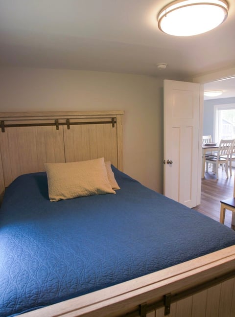 Cozy bedroom with blue bedspread, yellow pillow, wood barn door headboard, white closet, and ceiling light