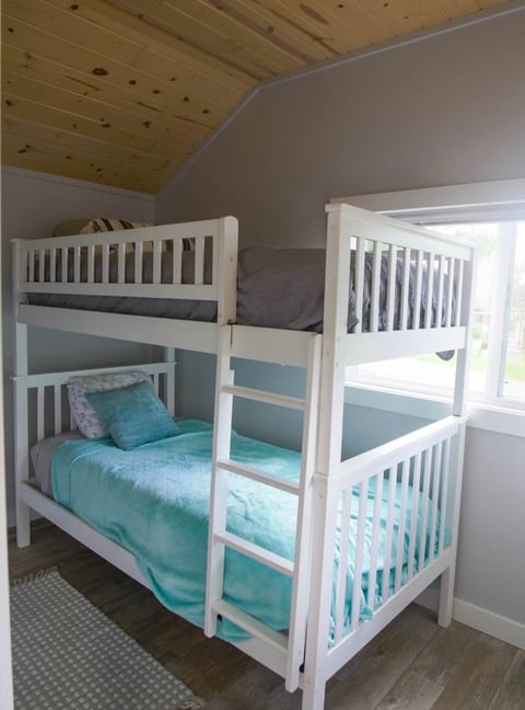 White bunk bed with turquoise bedding in a bedroom with wood ceiling and gray walls