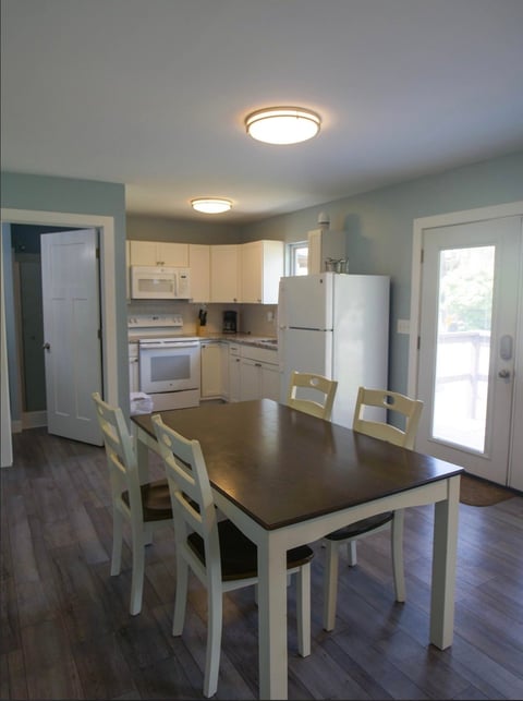 Spacious kitchen and dining area with cream cabinets, white appliances, dining table with chairs, and hardwood flooring