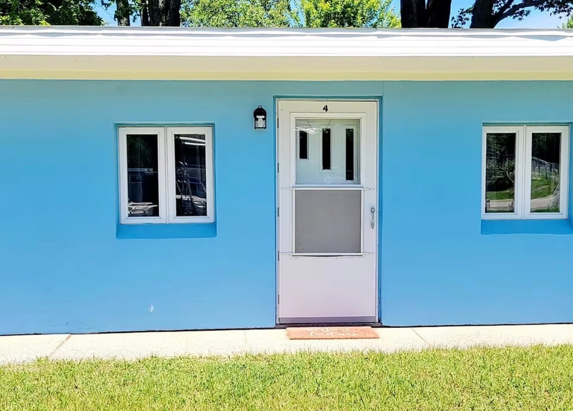 Bright blue house exterior with white trim, centered purple door, two windows, and green lawn