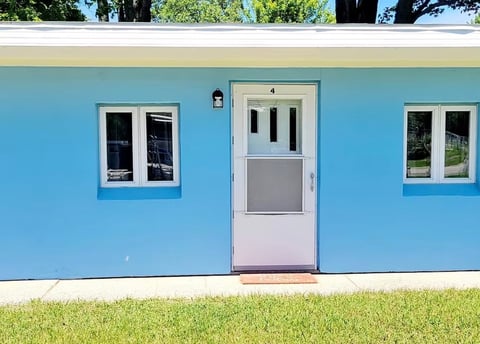 Bright blue house exterior with white trim, centered purple door, two windows, and green lawn