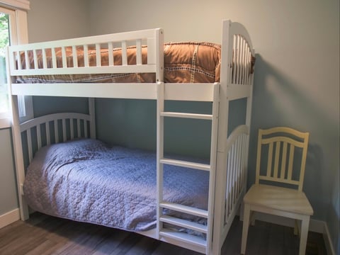 White wooden bunk bed with blue and orange bedding in a bedroom with hardwood floor and teal wall