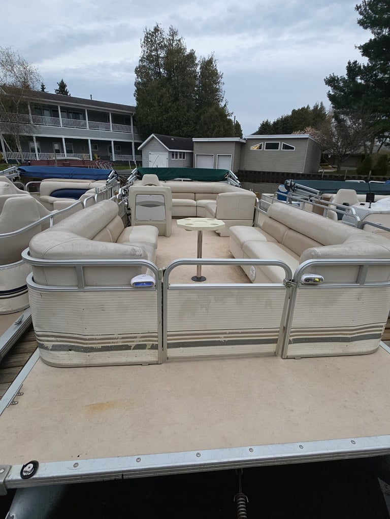 Beige pontoon boat interior with padded seating at a marina