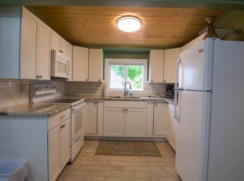 Modern kitchen with white cabinets, stainless steel appliances, wood ceiling, and tile flooring