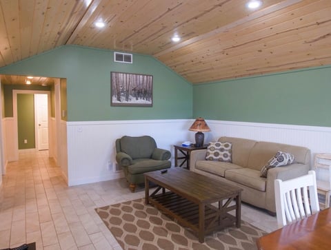 Modern living room with two-tone walls, wood ceiling, green armchair, beige sofa, wooden coffee table, and geometric area rug