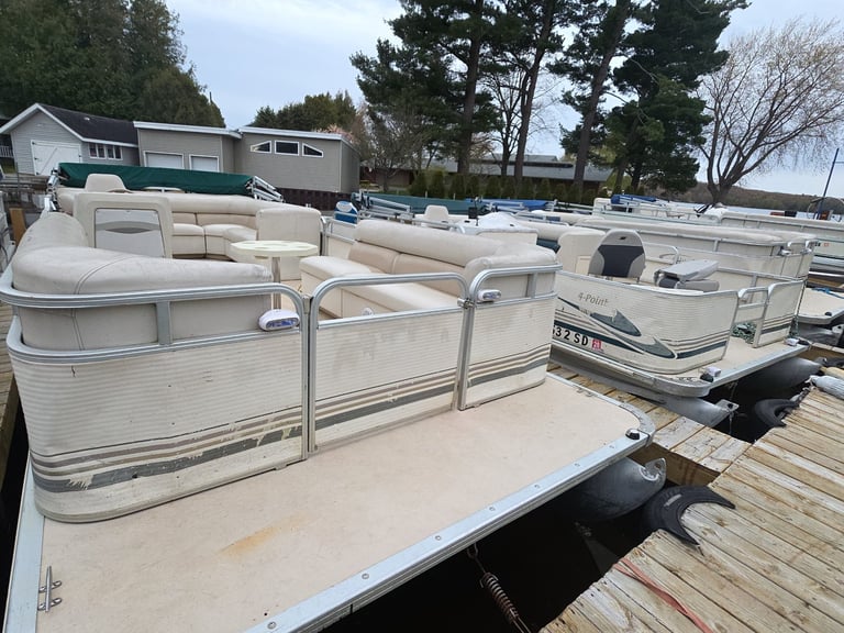 Beige pontoon boats docked at a wooden marina with trees and buildings