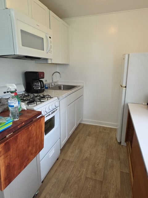 Small kitchen with white cabinets, gas stove, microwave, sink, refrigerator, and wood-grain flooring