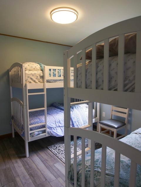 Modern childrens bedroom with two white loft bunk beds, hardwood flooring, and a round ceiling light fixture