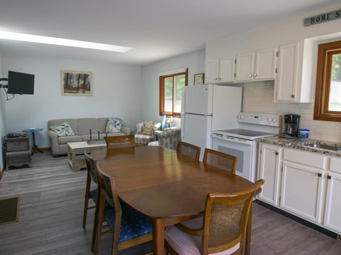 Open concept kitchen and dining area with wooden table, white cabinetry, appliances, and seating area in background