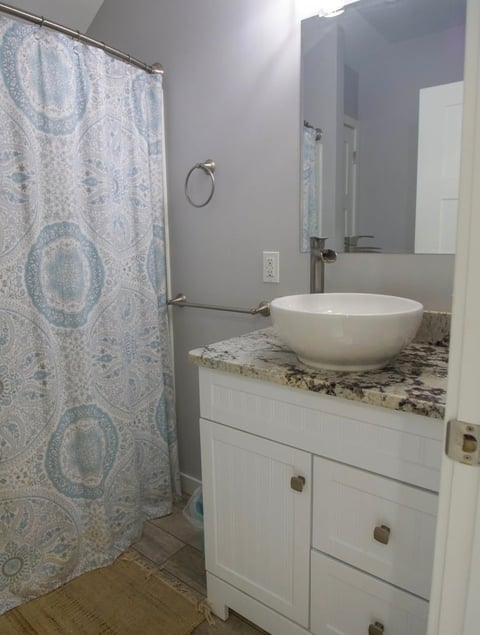 Modern bathroom with white vanity, round vessel sink, granite countertop, patterned shower curtain, and mirror