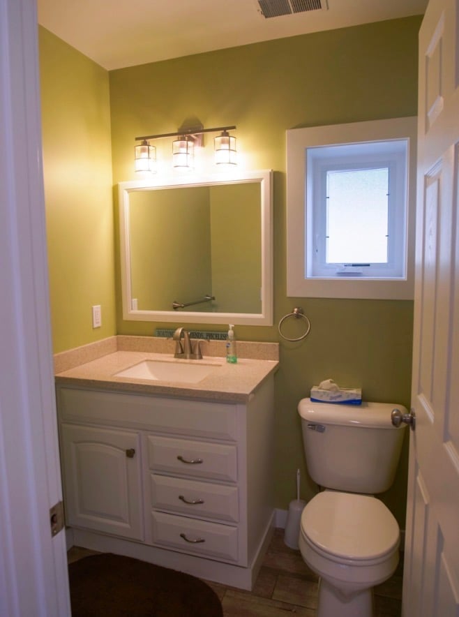 Modern bathroom with white vanity, large mirror, three-bulb light fixture, toilet, and green and cream colored walls